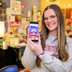 A smiling person holding their global campus graduation photo on their phone.