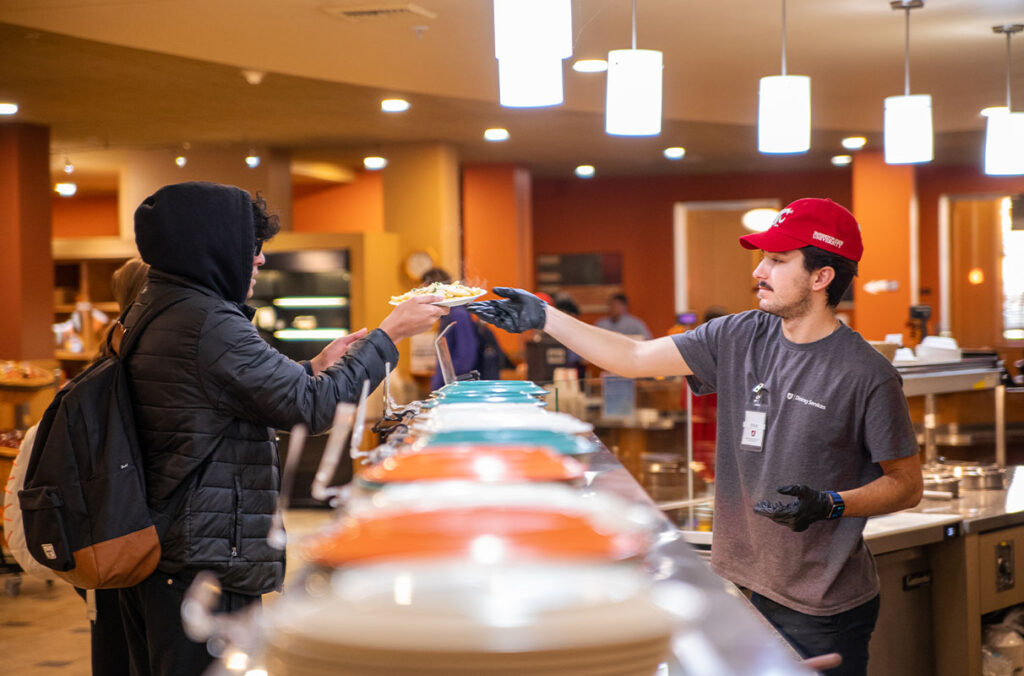 An employee hands a student a plate of food at Hillside Café.