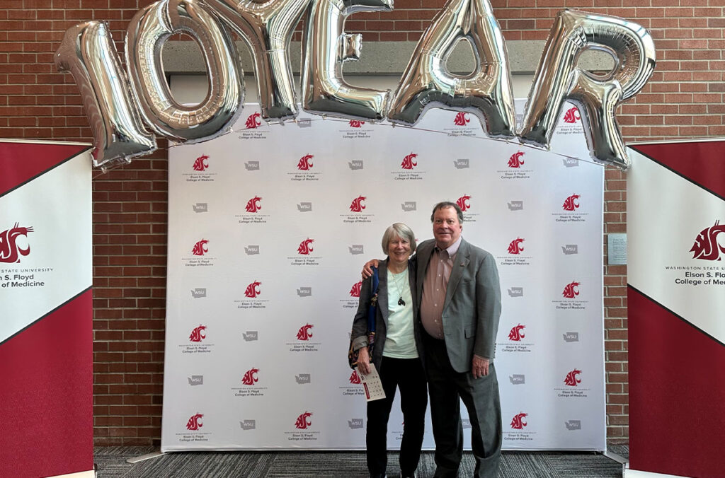 Barbara and Tom Wilson stand in front of a backdrop posing for a picture at an event commemorating the 10 year anniversary of the WSU College of Medicine.