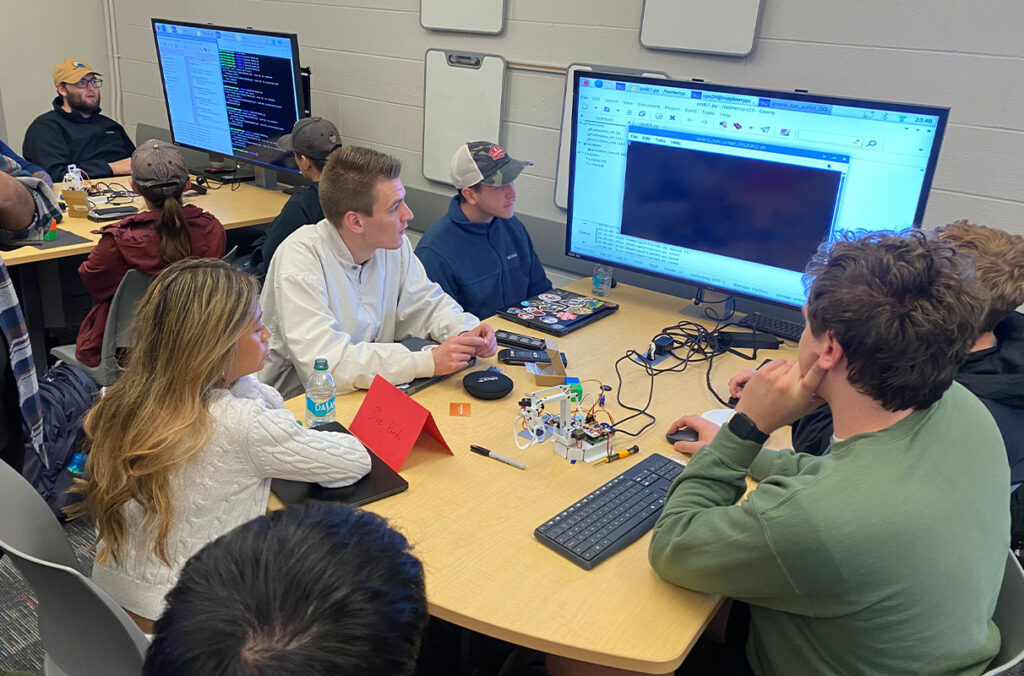 A group of people talk at a table while looking at a computer screen.