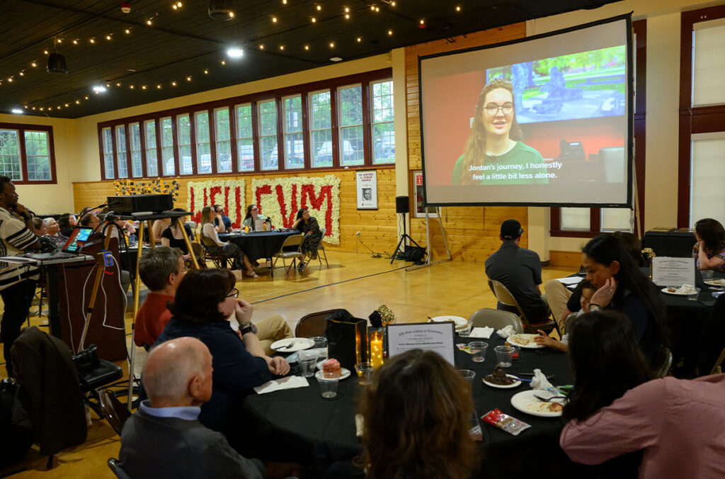 A group of people in a conference room watch a video recognizing outstanding students, faculty, and staff.