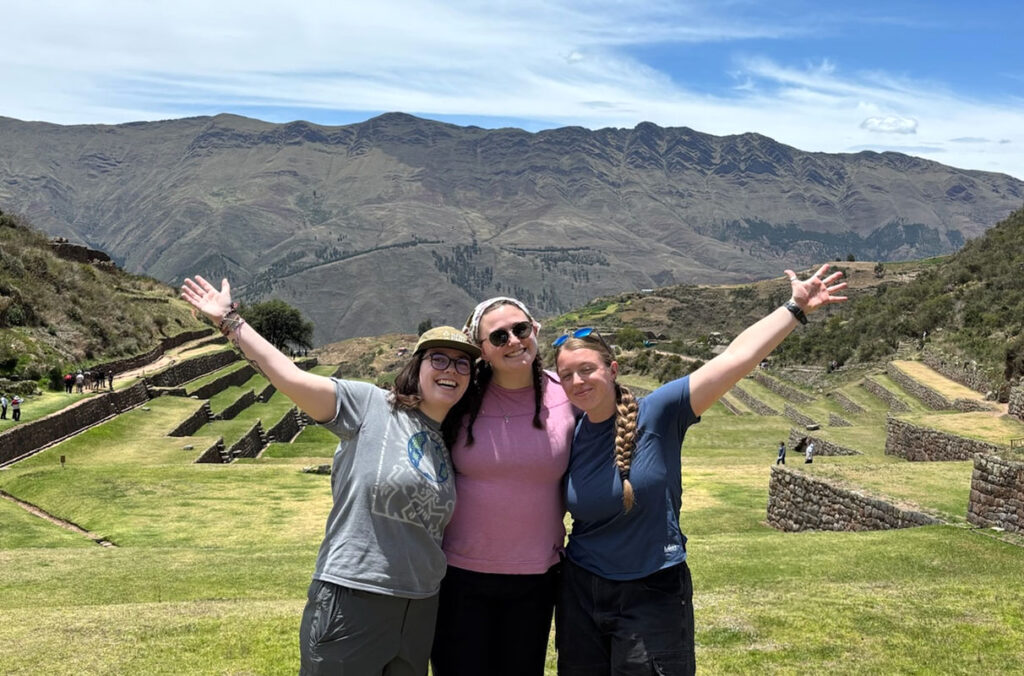 Three WSU students posing together on a grassy terrace inside the ancient ruins of Machu Picchu in Peru's Andes Mountains.