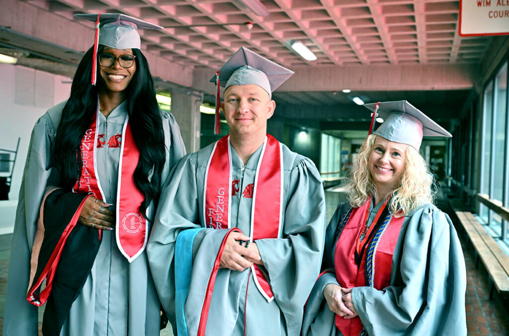 Three MHAL grads standing together in their caps and gowns in an empty hallway.