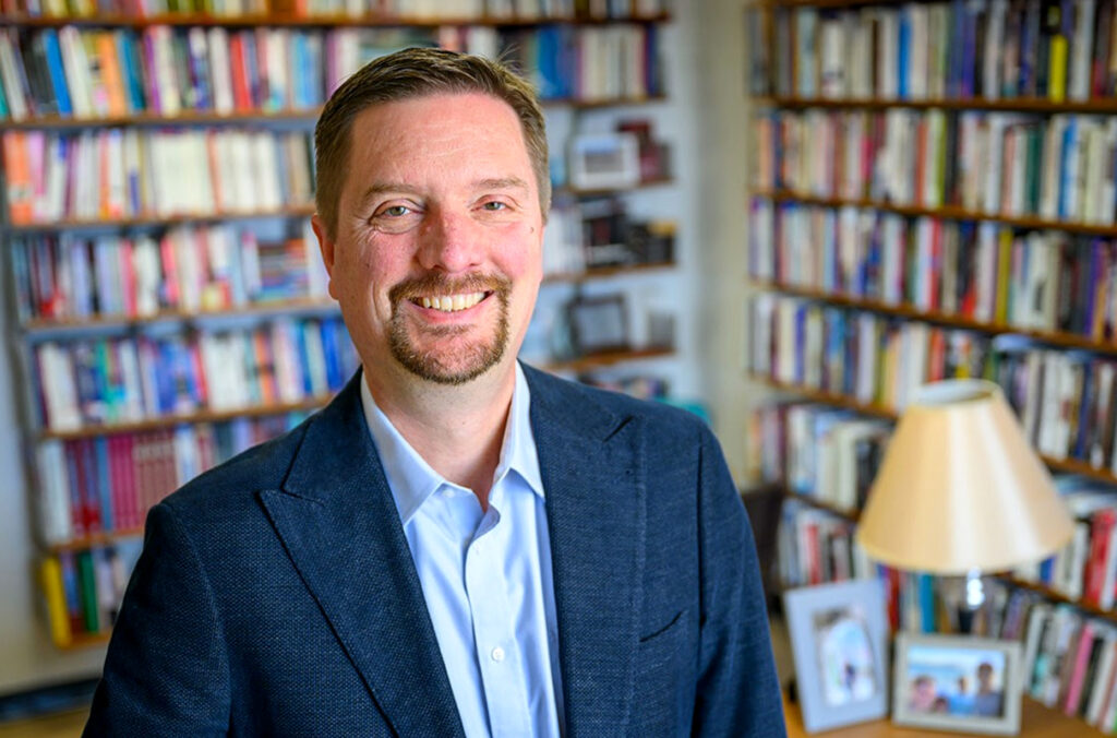 Matthew Sutton standing in his office before two bookcases.