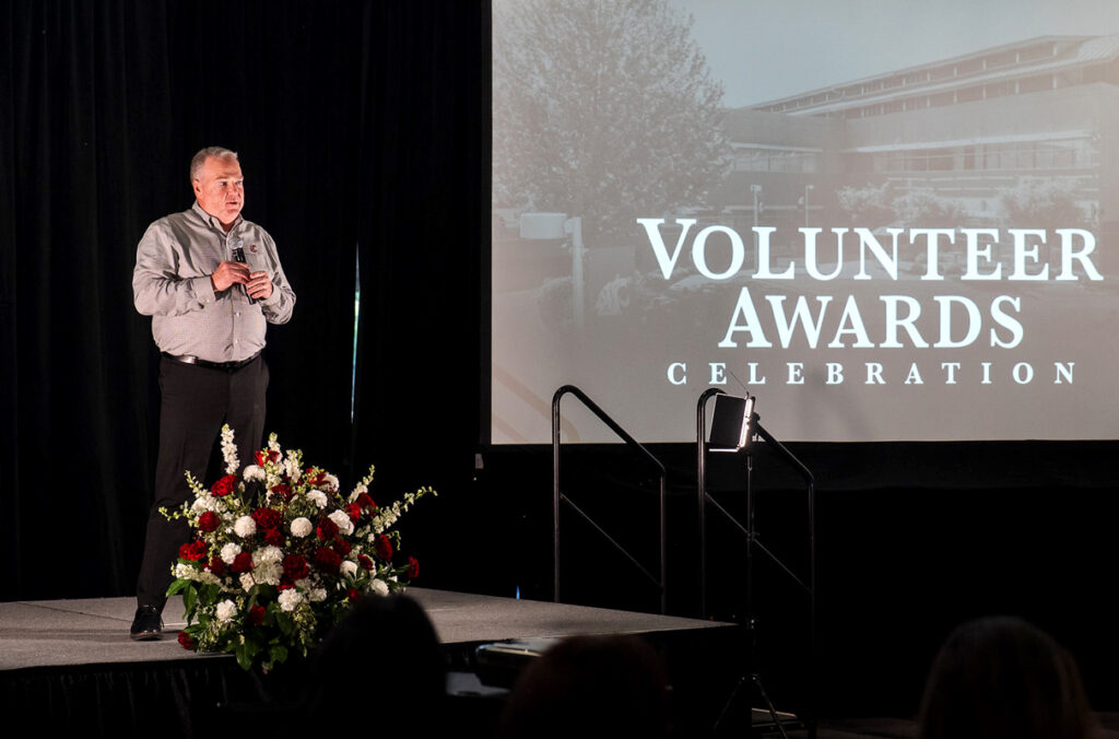 Mike Connell on stage next to a large display screen which reads "Volunteer Awards Celebration".