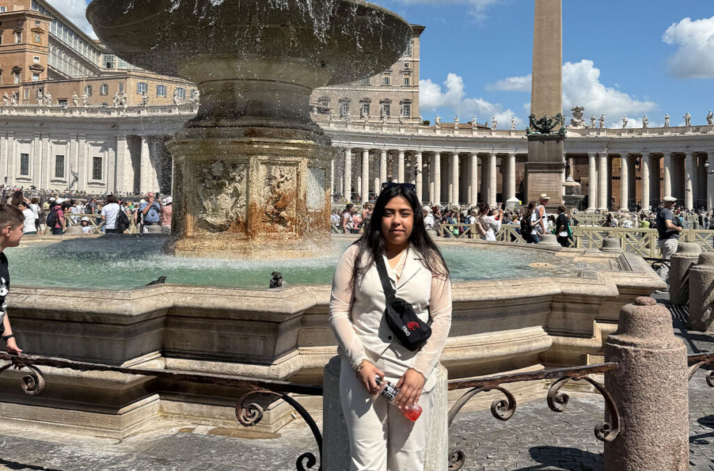 A woman stands in front of a fountain in Vatican City.
