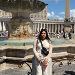 A woman stands in front of a fountain in Vatican City.