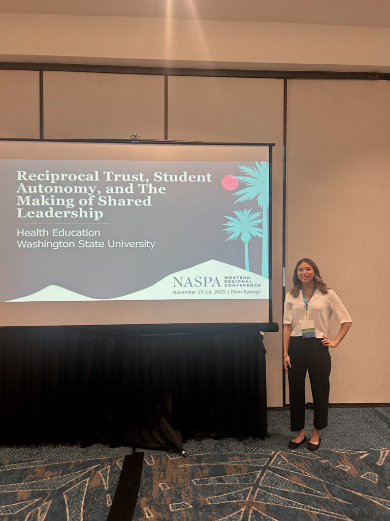A person stands next to a large screen that says “Reciprocal Trust, Student Autonomy, and The Making of Shared Leadership: Health Education, Washington State University.”