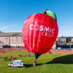 A hot-air balloon shaped like a crimson apple with the word Cosmic Crisp on it.