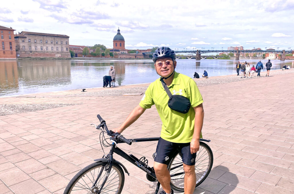 Bin Yang poses next to his bicycle in front of a waterway in Toulouse, France.