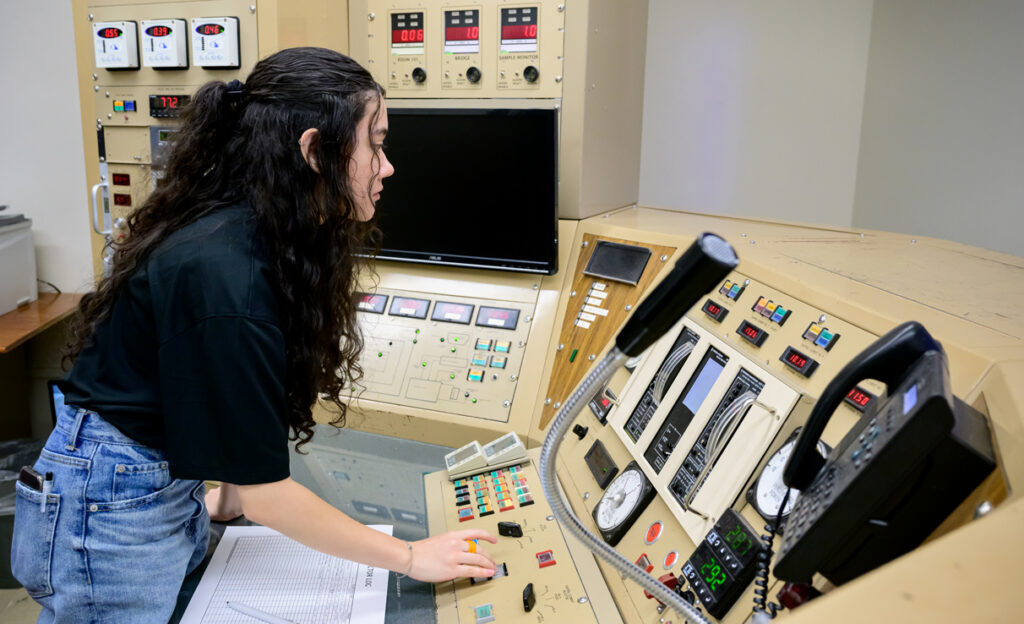 A student employee checks settings inside the control room of a research nuclear reactor.