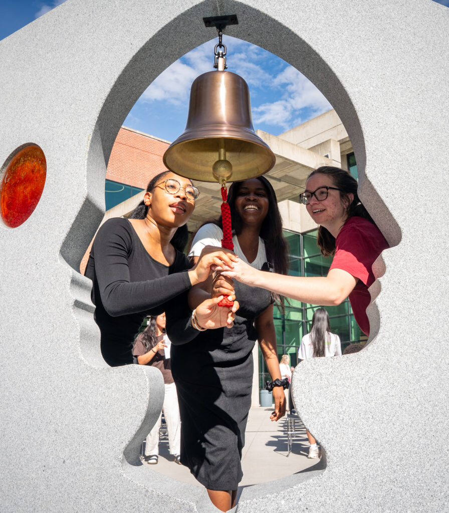 Three WSU students ringing the bell in the Pages of Care sculpture.