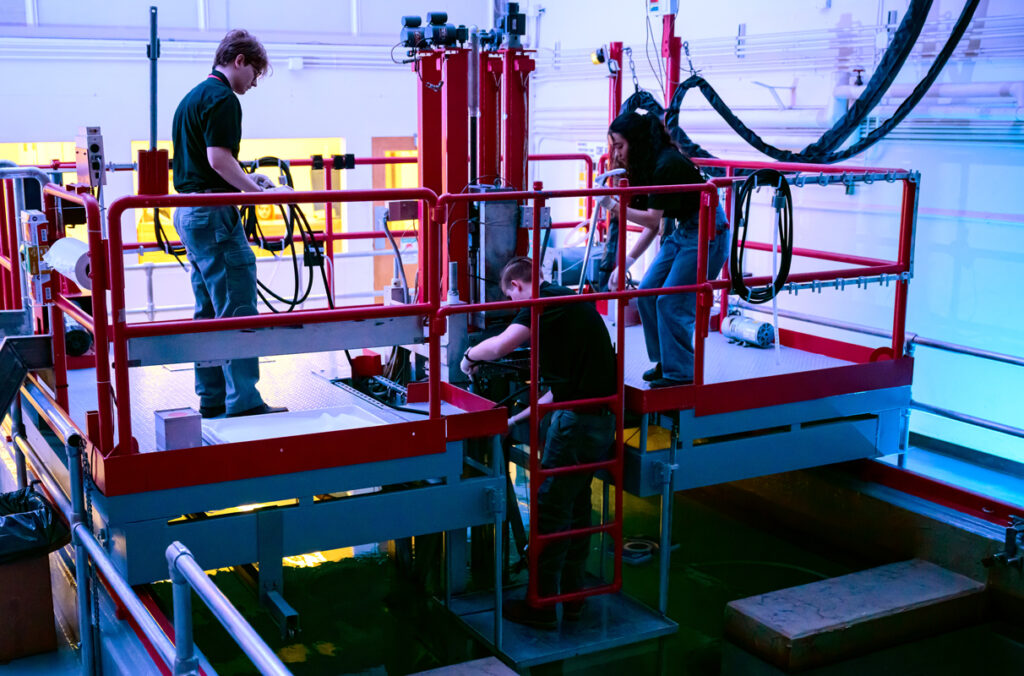Three people working on a raised platform inside a research nuclear reactor.