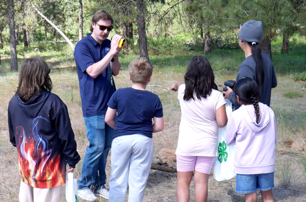 An adult educator demonstrates how to use a tool to a five youth at Owhi Lake.