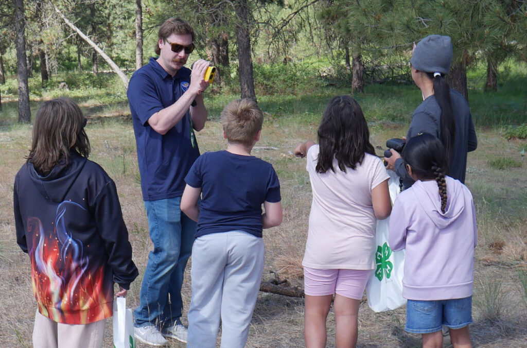 Adult educator demonstrates how to use a tool to a group of five youth.