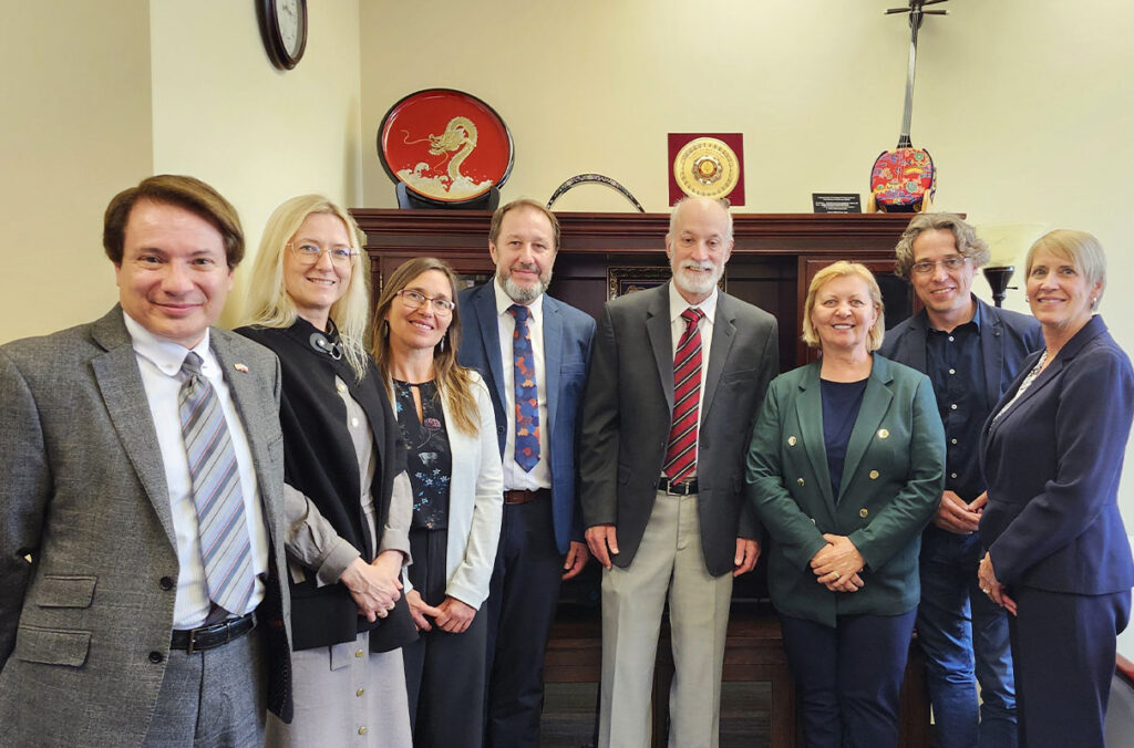A group of eight Washington State University and AGH University of Krakow representatives stand together in a formal office setting, dressed in professional attire, smiling at the camera.