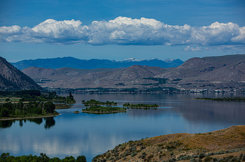 Image of serene lake with orchards and mountains in the background.