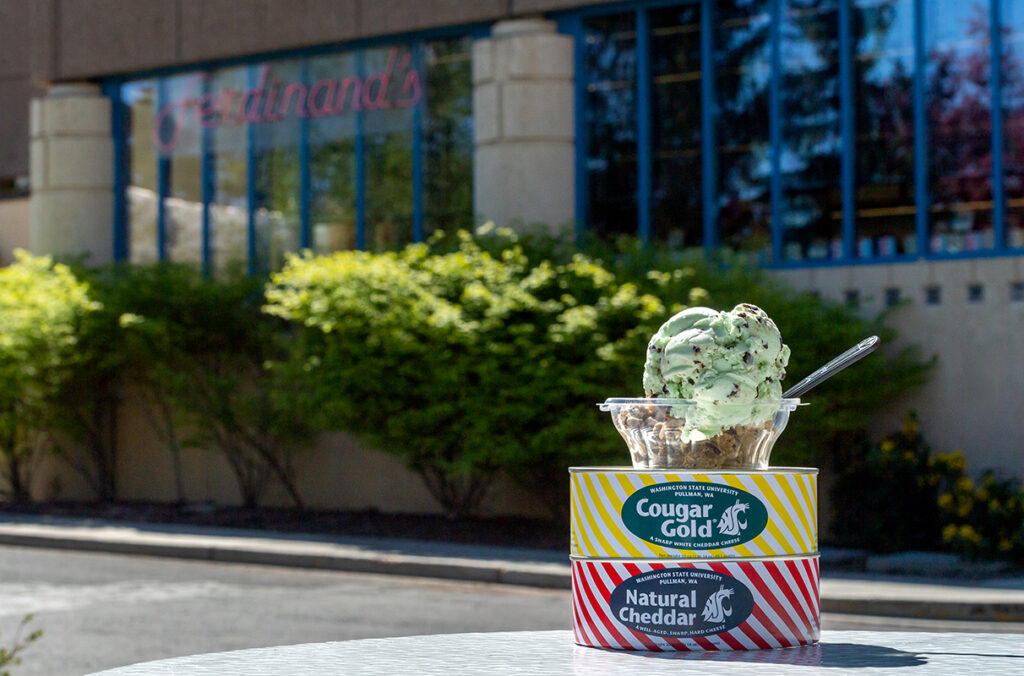 A bowl of ice cream sits atop two cans of cheese on a table outside of Ferdinand's Ice Cream Shoppe.
