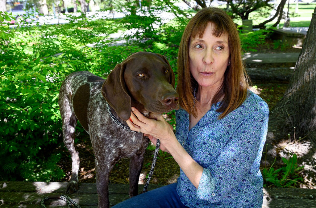 WSU researcher Katrina Mealey kneeling next to her dog, Cisco, under a tree.