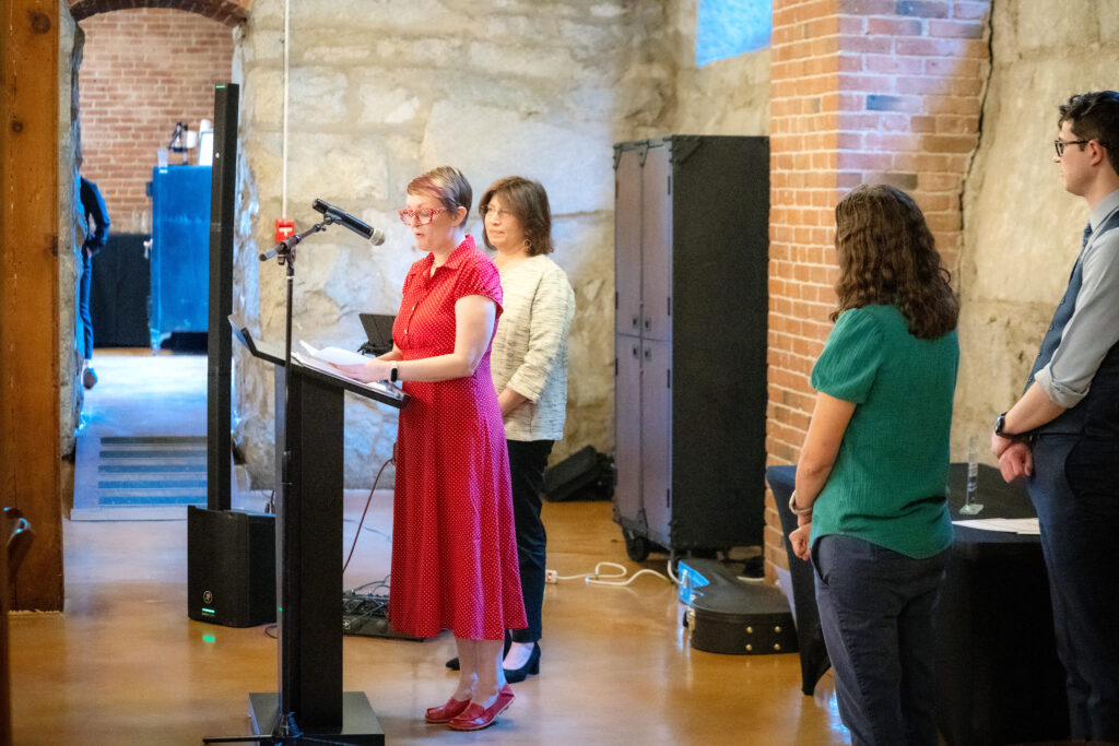 A woman accepts an award on a stage while other people look on.