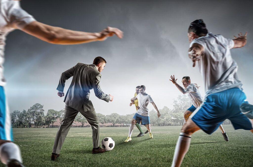 An illustration depicts a businessman in a suit playing soccer among players in uniform.