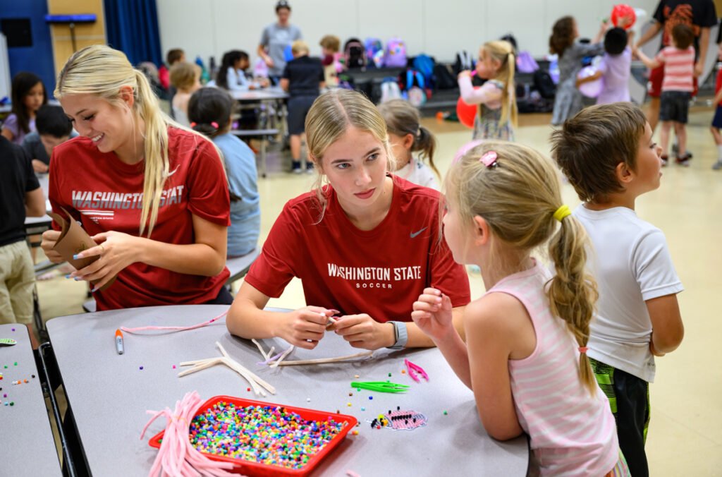 Two WSU student-athletes sit at a craft table making crafts with elementary school children.