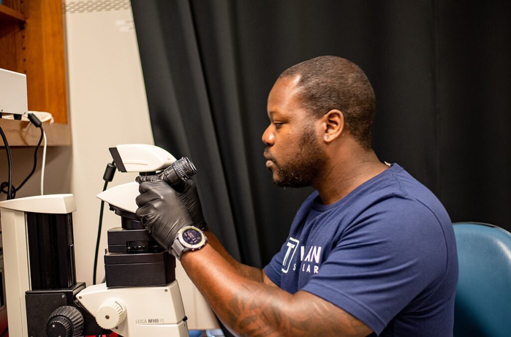 A researcher examines slides under a microscope.