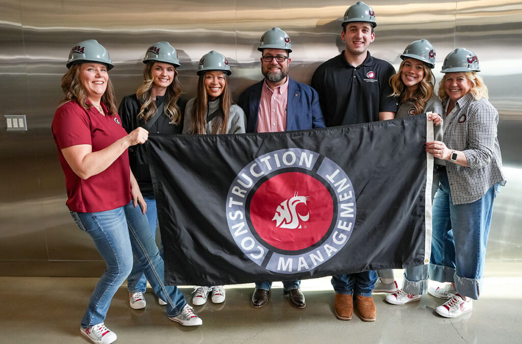 A group of construction management students stand in a line holding a flag that says construction management.