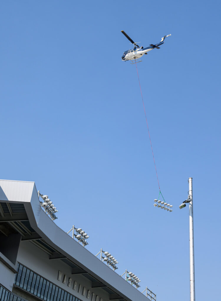 A helicopter flies over the press box carrying a light fixture out of Gesa Field.
