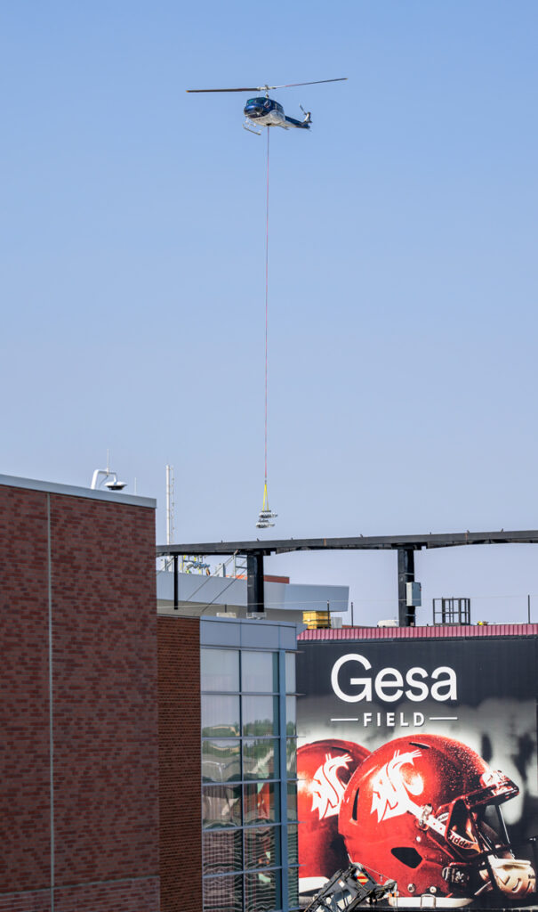 A helicopter flies over the scoreboard carrying a light fixture out of Gesa Field.