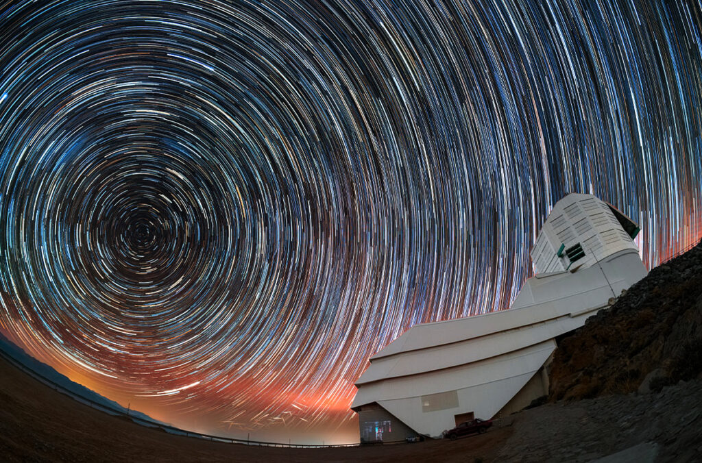 Star trails can be seen circling above an observatory in a long exposure image.