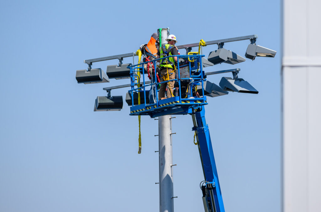 Two workers on a boom lift install a new LED light fixture after it was delivered via helicopter.