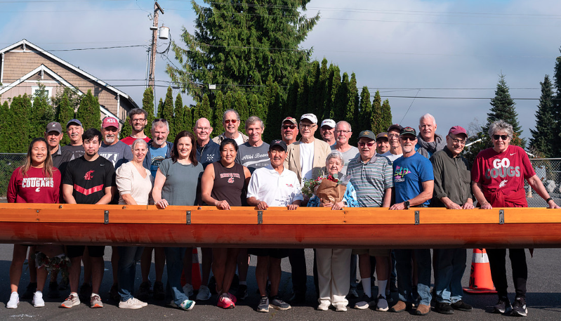 People gather behind a racing shell for a photo.