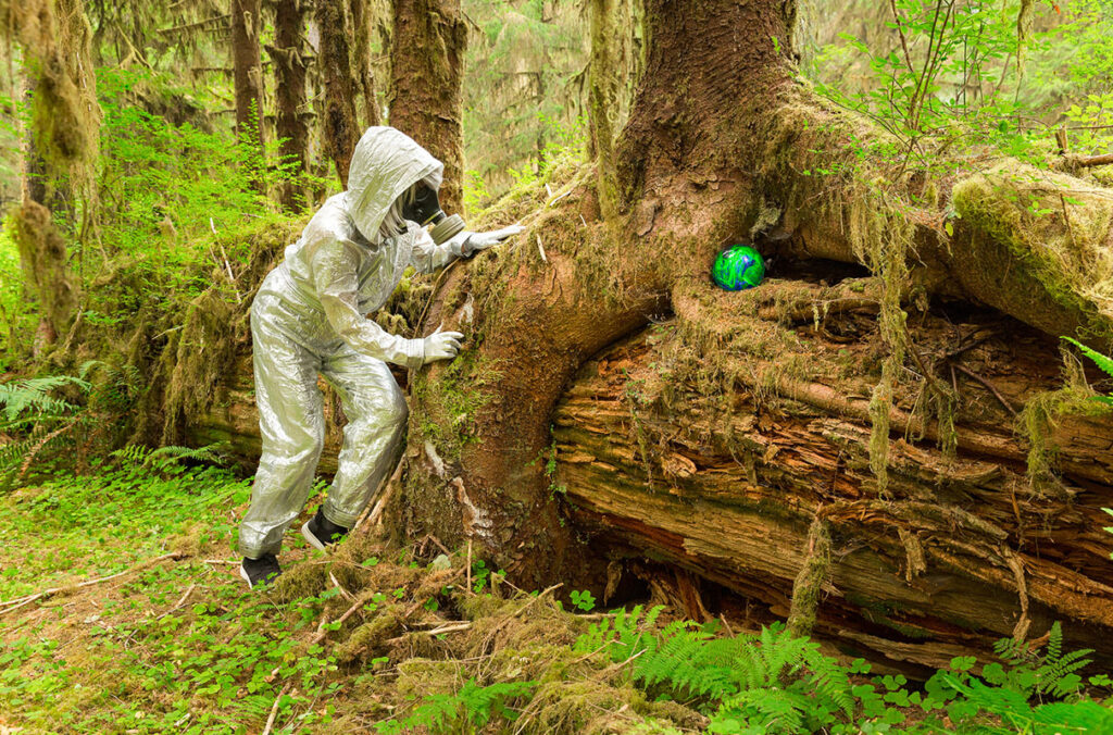 A photograph of a man in a spacesuit looking at a bowling ball in a forest.