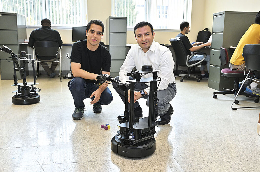 A student and professor pose with a robot in a laboratory.