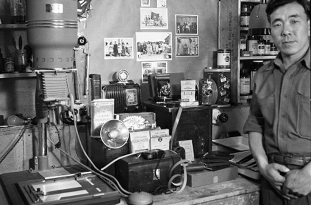 A man stands next to photography equipment in a historical photograph.
