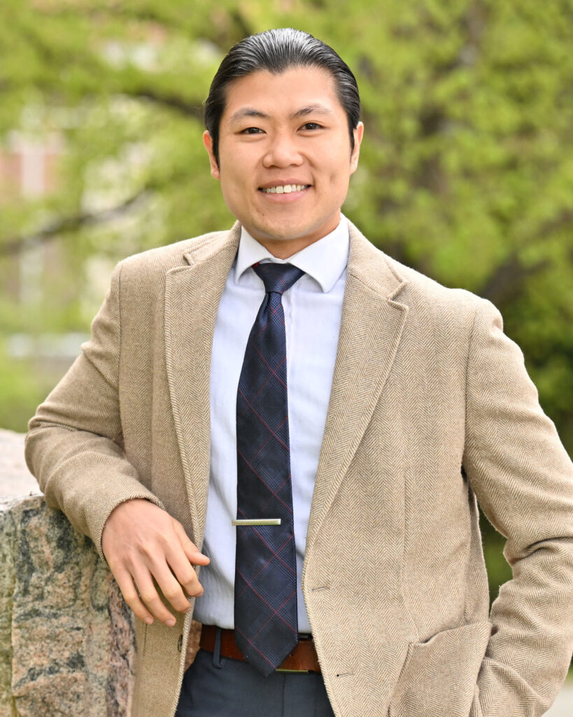 Professor poses outside in a suit and tie.