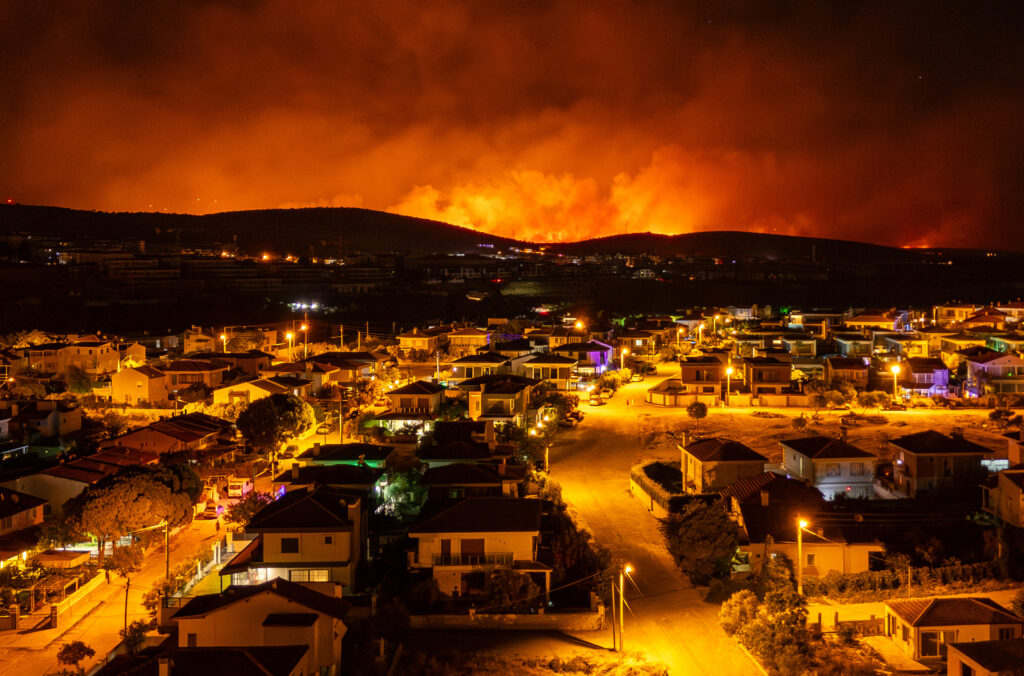 A wildfire burning on a distant hill threatening a residential neighborhood below.