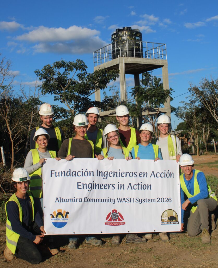 engineering students pose for a photo with their new water distribution system in the background