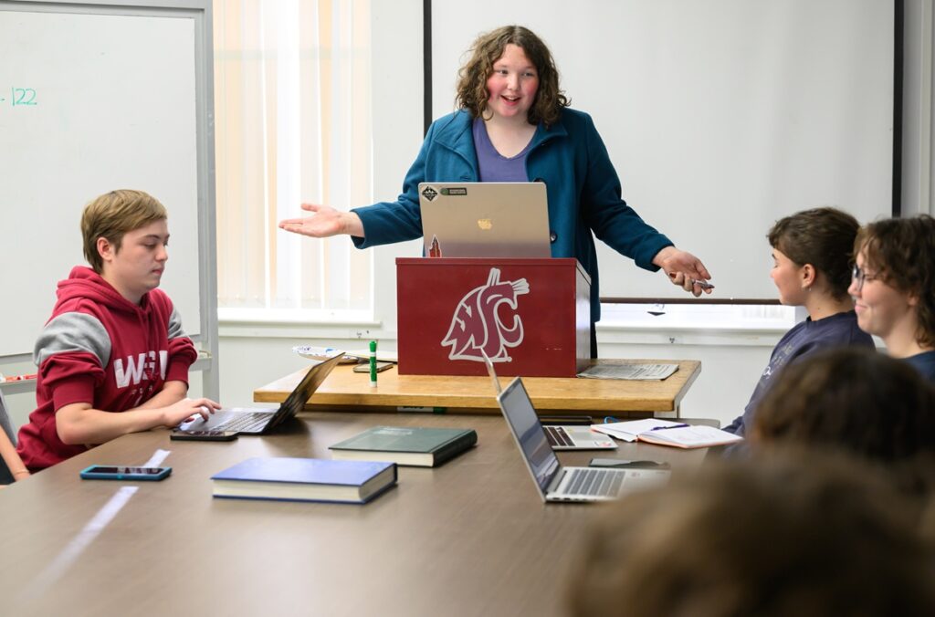 Lucy Stutesman stands at a podium during a meeting of Daily Evergreen staff