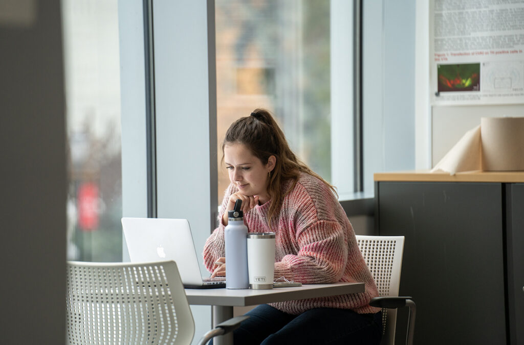 Student in pink sweater seated, looking at laptop on WSU Spokane campus.