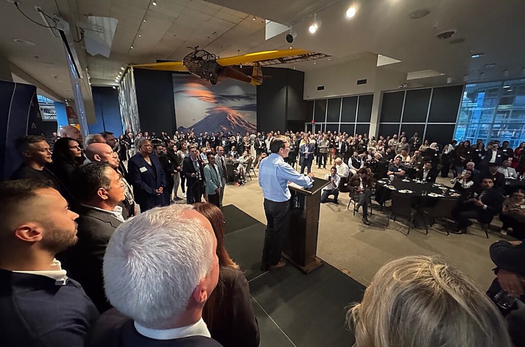 Washington Gov. Bob Ferguson stands at a podium addressing a large crowd.