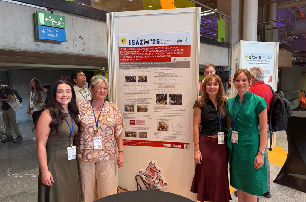 4 people stand around a large academic poster in a big open area.