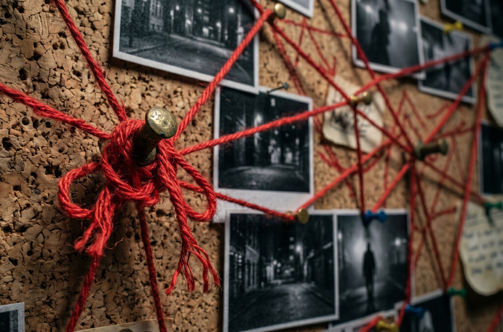 A crime board is covered with pictures and string connecting bits of information together.