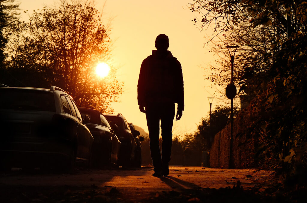 A person walks down a city street at sunset.