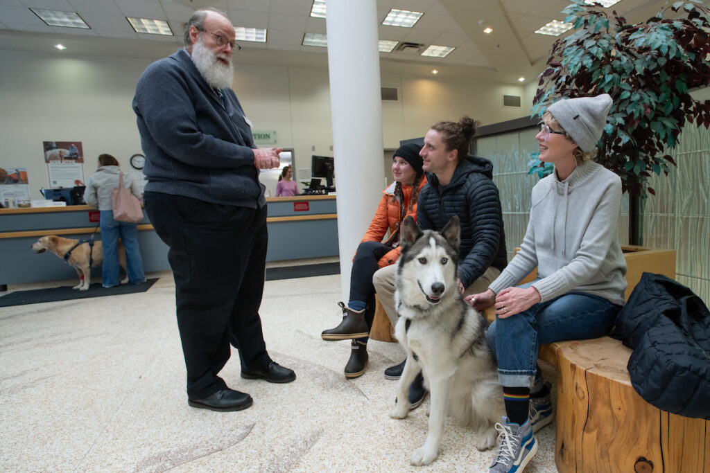 Scott Campbell, left, the veterinary chaplain at Washington State University's College of Veterinary Medicine, visits with Olivia and Phinehas Lampman, center, owners of Goose, a Husky mix dog, as Phinehas’ mother and WSU Honors College Associate Professor Annie Lampman, right, looks on, Wednesday, Jan. 10, 2024, in the lobby of the Veterinary Teaching Hospital in Pullman.
