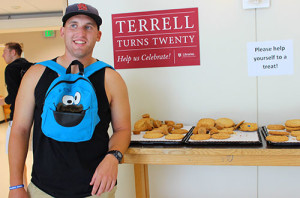 A student with a Cookie Monster-themed backpack stands next to a table full of cookies.