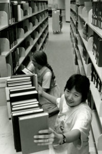 A black and white photo of two women shelving books at a library.