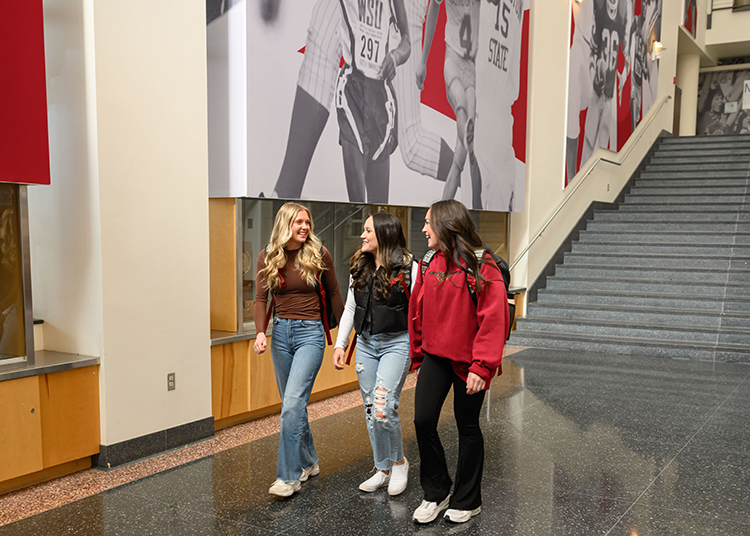 Three students walk through the WSU Athletic Hall of Fame building with their backpacks.