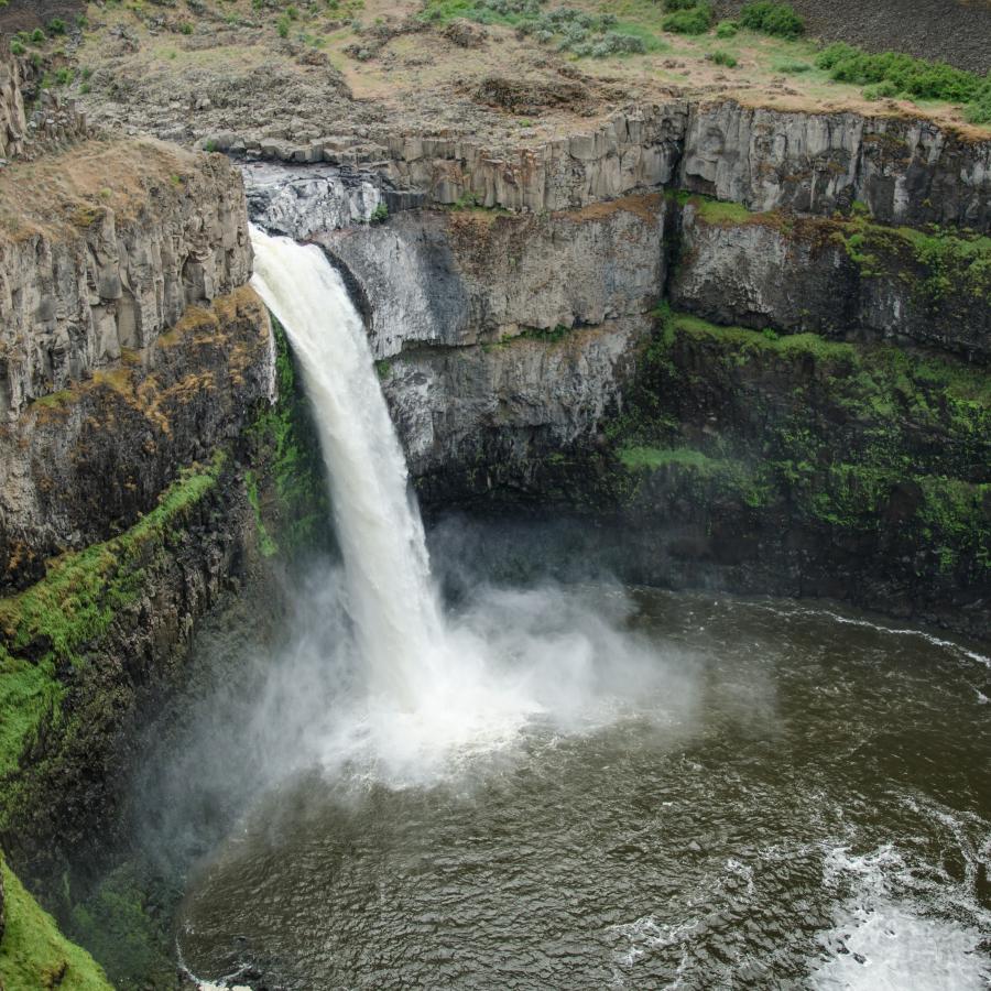 A waterfall over cliffs into a round lake.